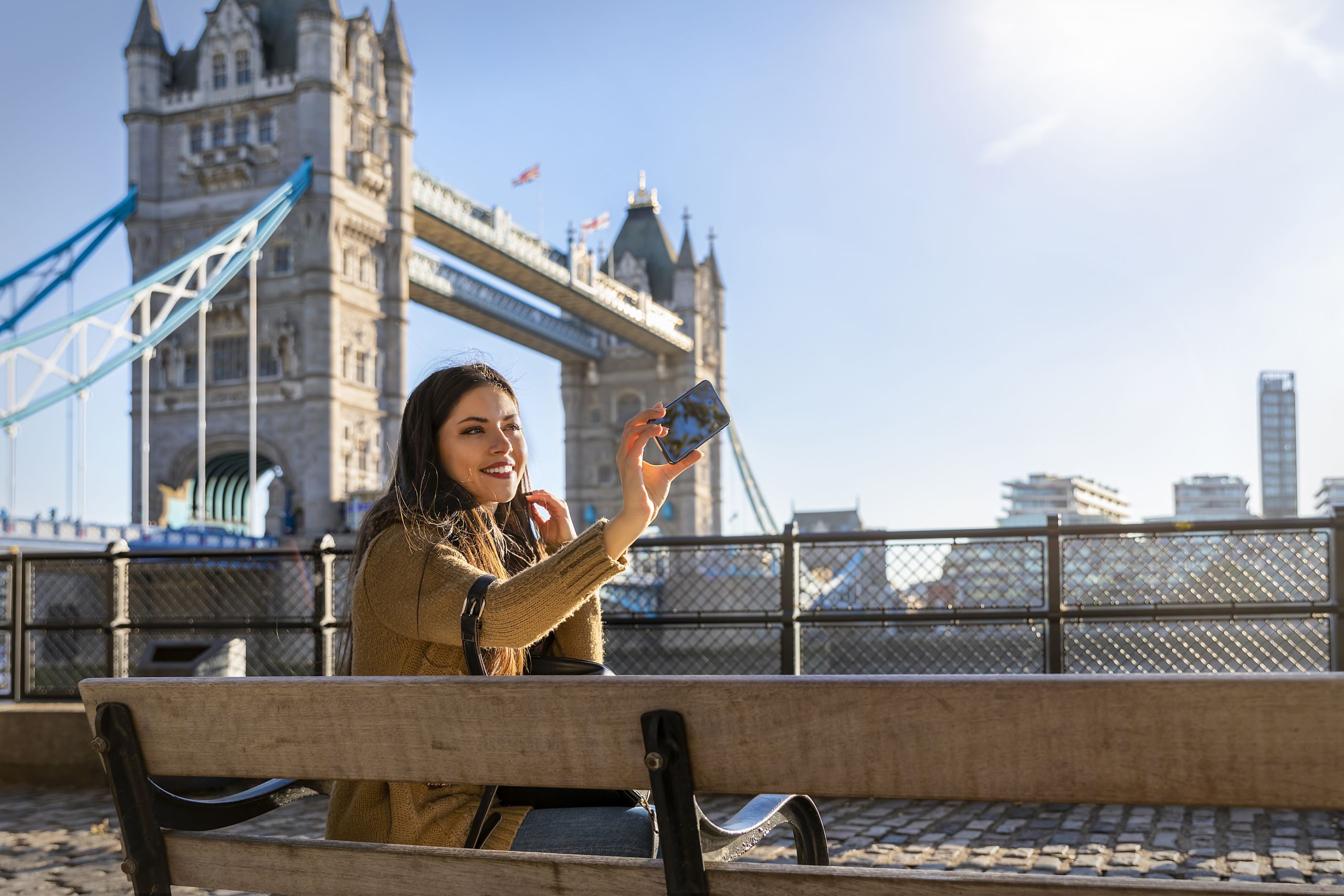 Female London traveler takes a selfie picture with her phone in front of the Tower Bridge